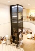 Senkrecht-Plattformlift in Möbelhaus über zwei Etagen mit verglastem Liftschacht